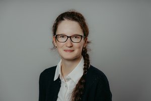 Porträt einer jungen Frau vor dunklem Hintergrund, frontal fotografiert und freundlich lächelnd.