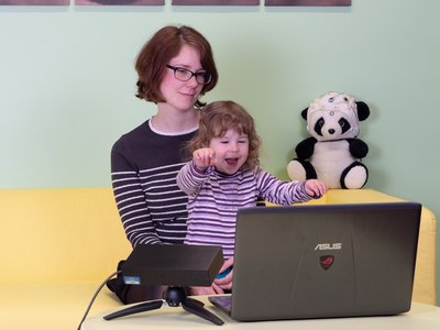 Kind sitzt bei der Mutter auf dem Schoß und schaut auf einen Laptop