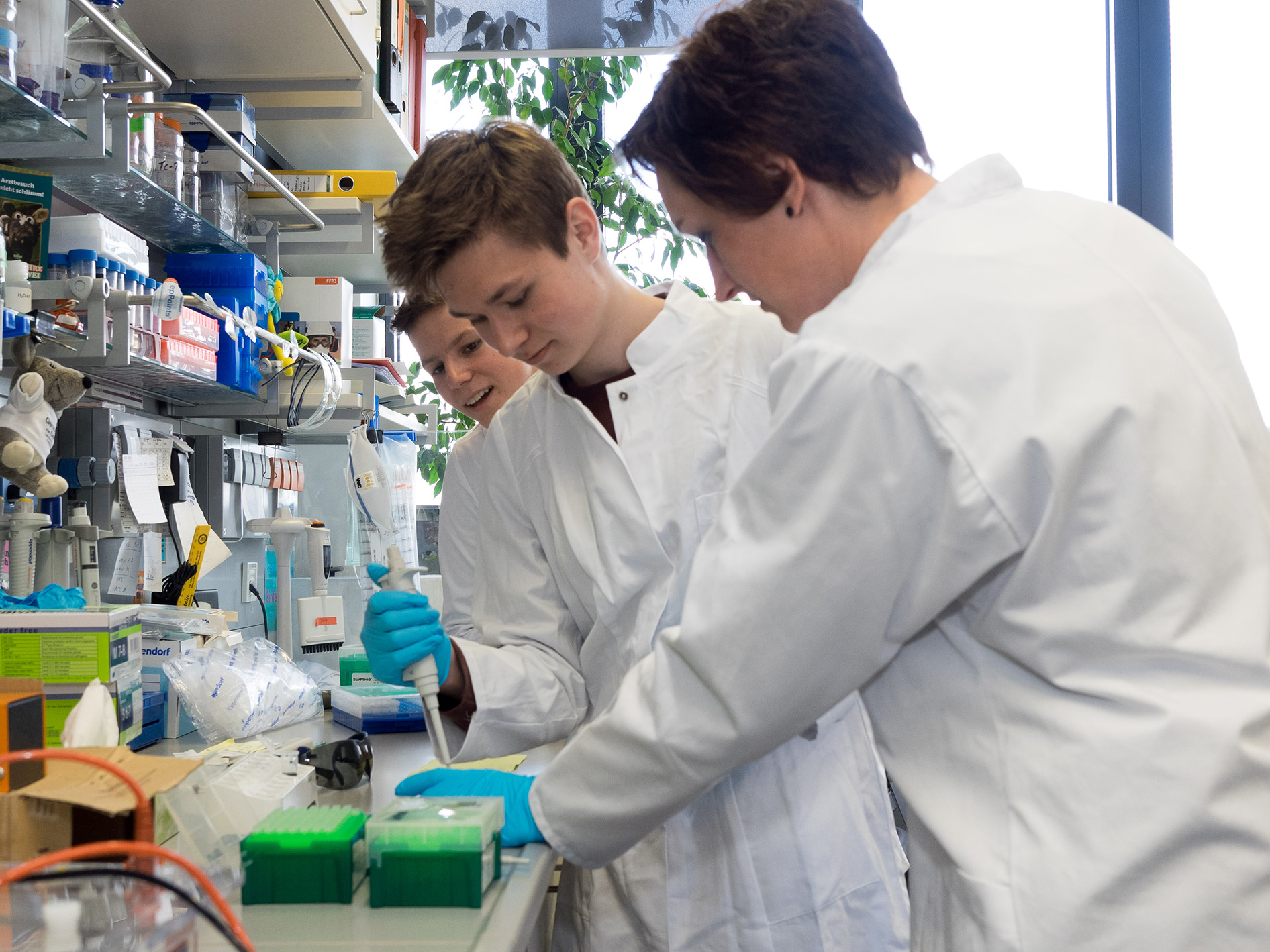 2 Teilnehmer des Boys Day im Labor mit Technischer Assistentin, die das Pipettieren zeigt