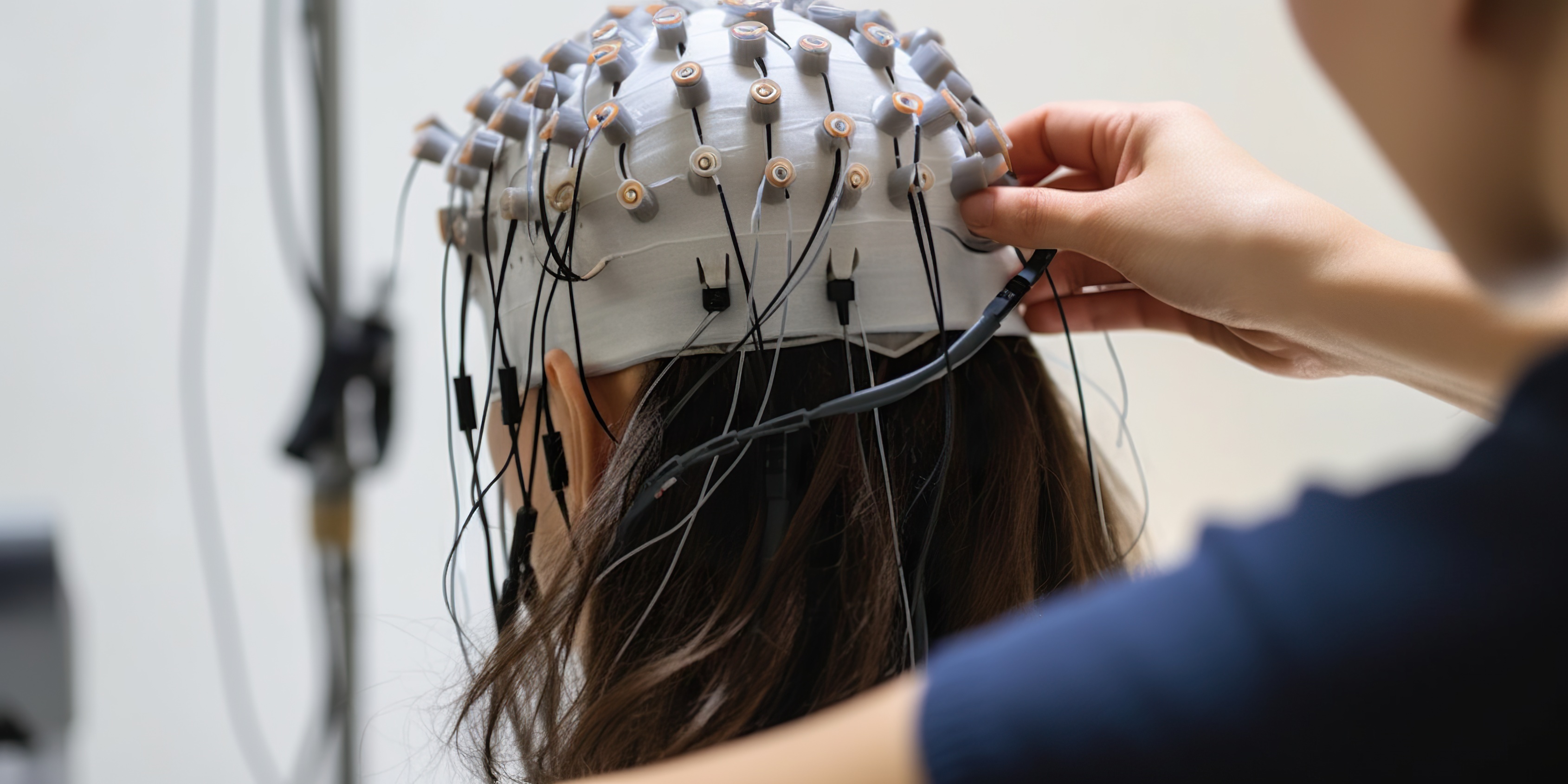 Forschende setzen einer Probandin eine EEG-Haube mit zahlreichen Elektroden auf, um Gehirnaktivität zu messen