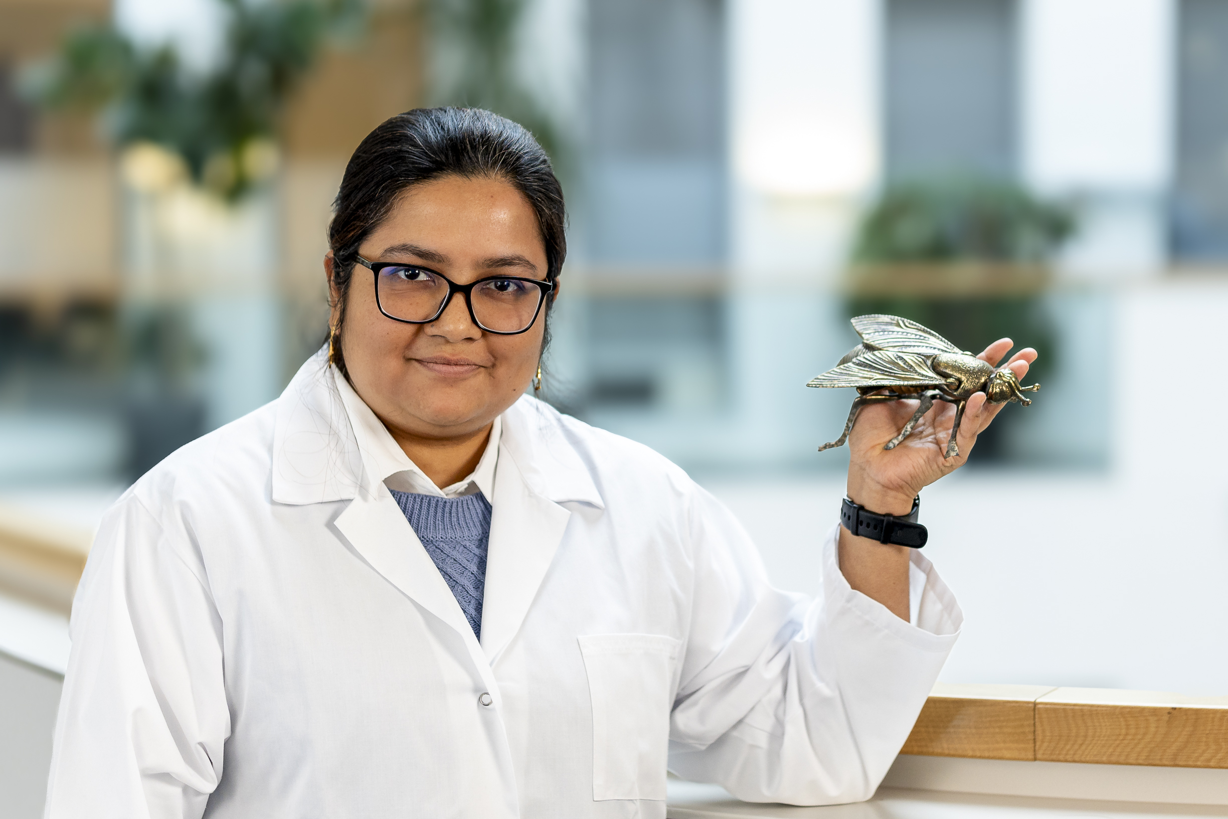 Fatima Amin hält in ihrer linken Hand das Modell einer Drosophila und lächelt in die Kamera.